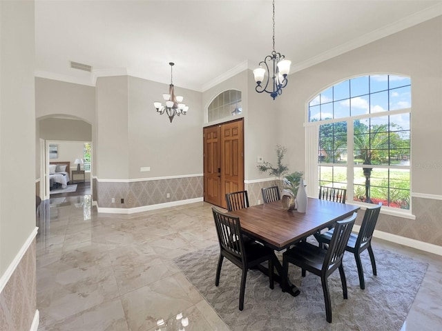 dining room with a chandelier, crown molding, arched walkways, marble finish flooring, and a wainscoted wall