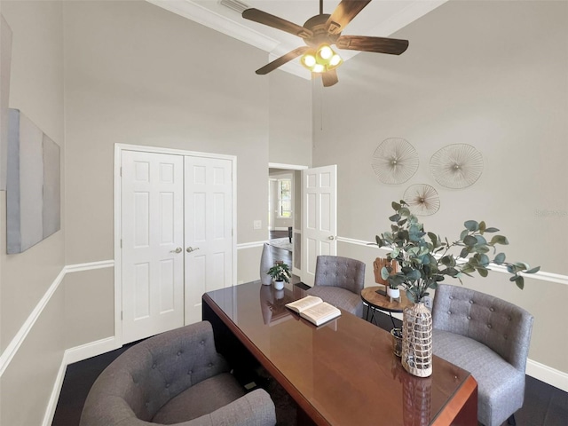 office area with a towering ceiling, baseboards, a ceiling fan, and wood finished floors