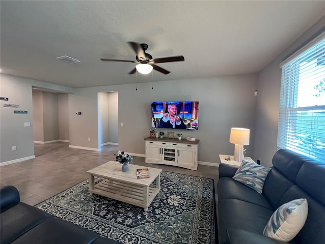 living area with visible vents, a textured ceiling, baseboards, and a ceiling fan