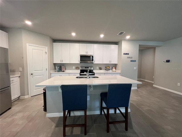 kitchen featuring visible vents, an island with sink, a sink, stainless steel appliances, and light countertops