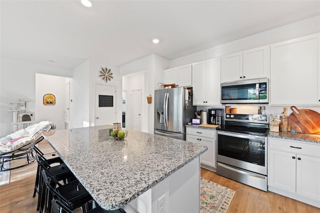 1153 Augustus Dr, Davenport, FL 33896 - kitchen featuring light wood-type flooring, a center island, white cabinets, light stone countertops, and appliances with stainless steel finishes