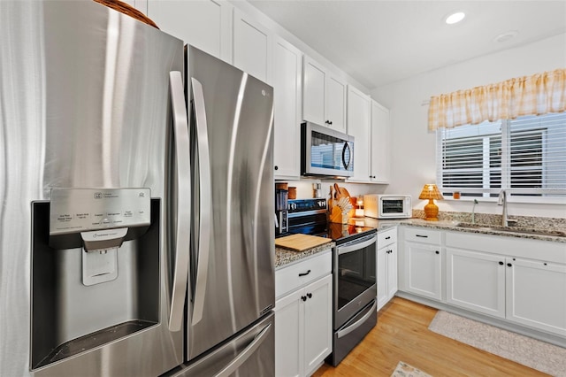 1153 Augustus Dr, Davenport, FL 33896 - kitchen featuring light wood-style flooring, white cabinetry, light stone counters, a sink, and stainless steel appliances