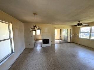 unfurnished living room featuring ceiling fan with notable chandelier, a fireplace, and speckled floor