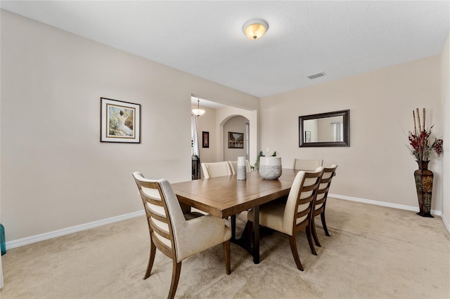 dining area with arched walkways, visible vents, light colored carpet, and baseboards