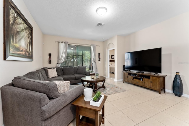 living room with light tile patterned floors, visible vents, baseboards, and a textured ceiling