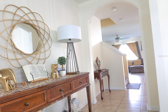 hall featuring baseboards, arched walkways, and light tile patterned floors