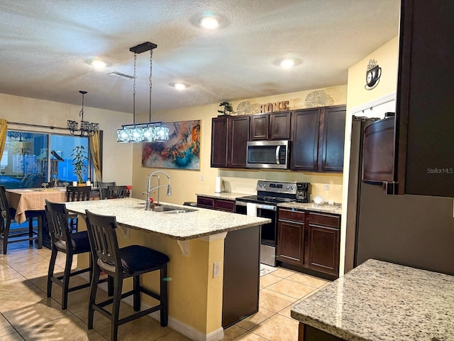 kitchen with a textured ceiling, a kitchen island with sink, stainless steel appliances, a sink, and a breakfast bar area