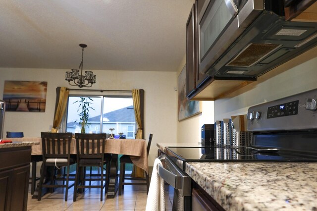 kitchen featuring light tile patterned flooring, a chandelier, light stone countertops, stainless steel appliances, and dark brown cabinetry
