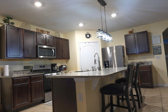 kitchen featuring a kitchen breakfast bar, light tile patterned floors, light stone counters, dark brown cabinetry, and appliances with stainless steel finishes