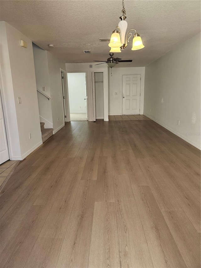 2921 Puerta Del Sol Blvd, Kissimmee, FL 34744 - unfurnished living room featuring visible vents, stairway, ceiling fan with notable chandelier, wood finished floors, and a textured ceiling