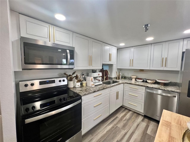 kitchen featuring light wood-style flooring, appliances with stainless steel finishes, a sink, and white cabinets