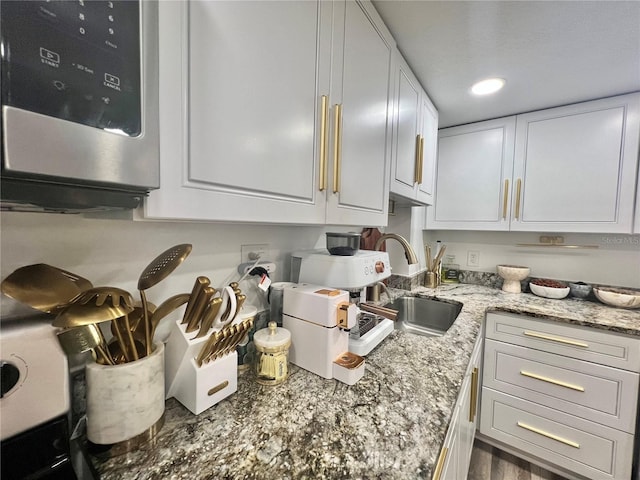 kitchen with recessed lighting, light stone countertops, white cabinetry, and a sink
