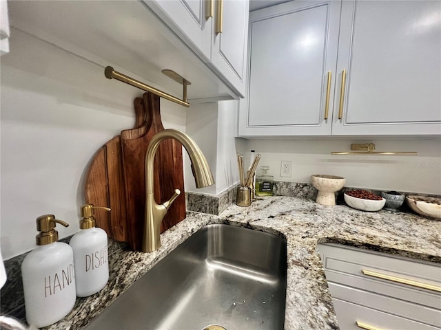 details featuring a sink, white cabinets, and light stone counters