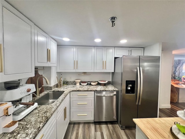 kitchen with white cabinets, a sink, dark wood-style floors, stainless steel appliances, and light stone counters