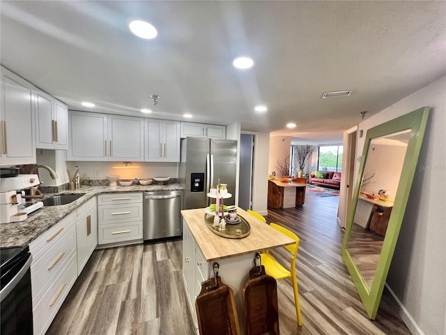 kitchen with white cabinets, appliances with stainless steel finishes, wood finished floors, a sink, and butcher block countertops