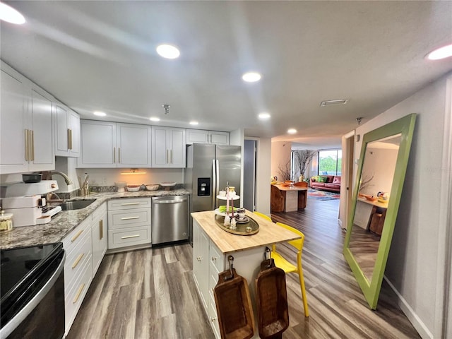kitchen with a sink, light stone countertops, wood finished floors, and stainless steel appliances