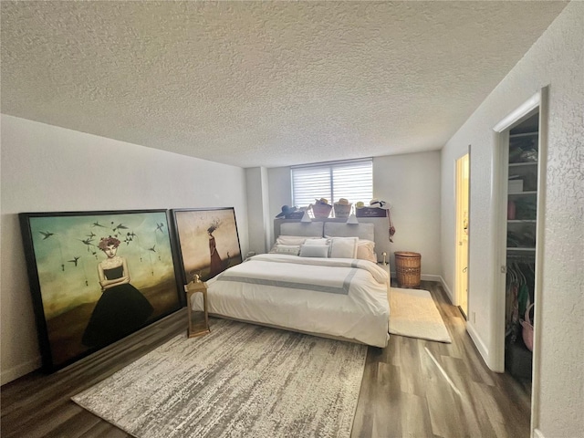 bedroom with a textured ceiling, baseboards, and wood finished floors