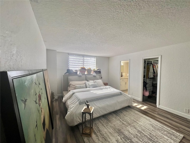 bedroom with a textured wall, a walk in closet, a textured ceiling, and wood finished floors