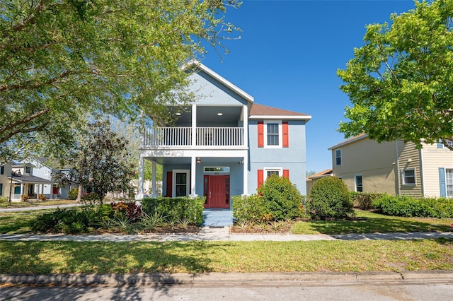 view of front of property featuring a balcony, a front lawn, and stucco siding