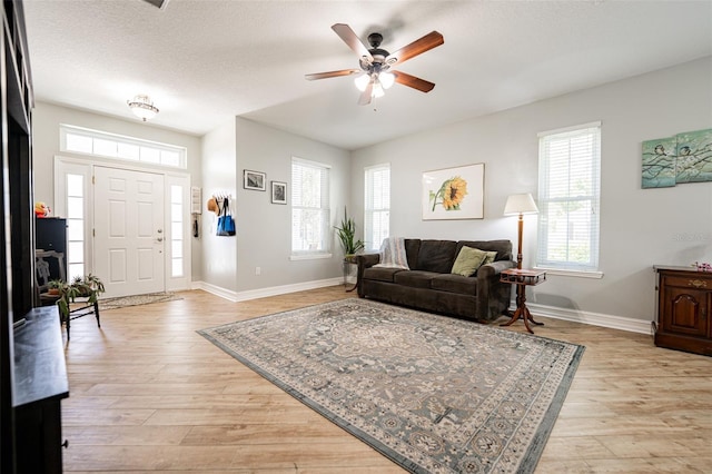 living room featuring baseboards, a textured ceiling, a ceiling fan, and light wood-type flooring