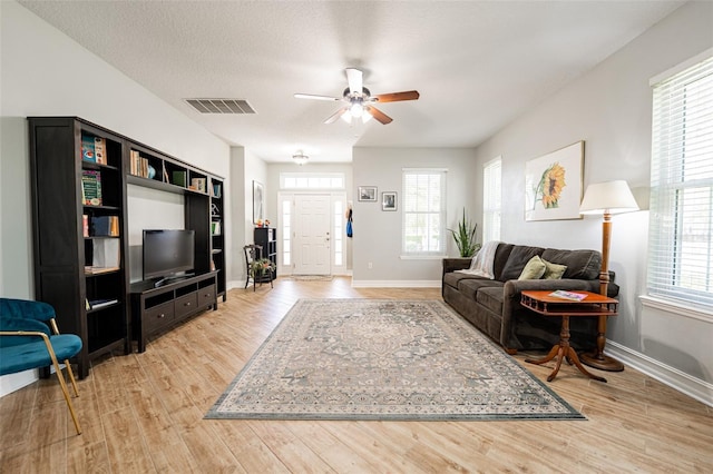living area featuring a textured ceiling, light wood-style flooring, baseboards, visible vents, and ceiling fan