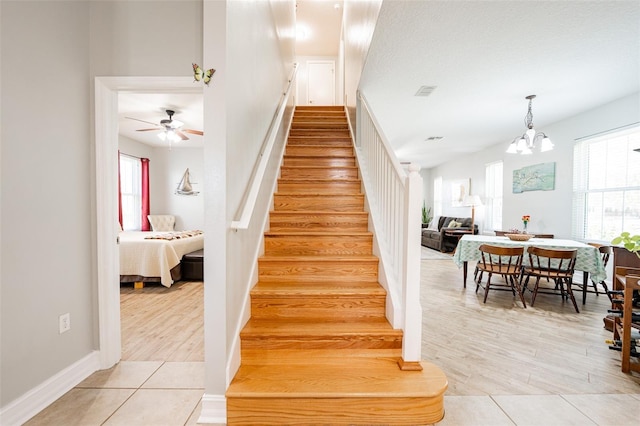 stairway featuring baseboards, visible vents, ceiling fan with notable chandelier, and wood finished floors