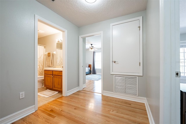 hallway featuring a textured ceiling, visible vents, light wood-style floors, and plenty of natural light