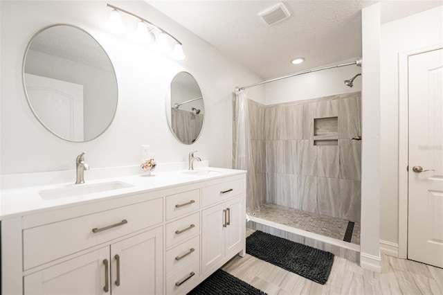 bathroom featuring double vanity, visible vents, a tile shower, and a sink