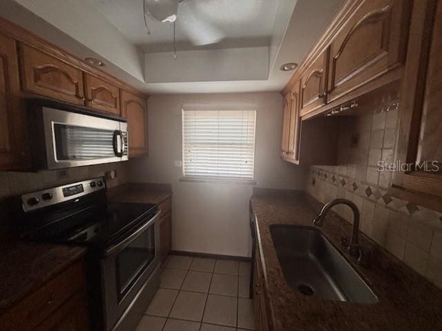kitchen featuring a sink, appliances with stainless steel finishes, a tray ceiling, and dark countertops