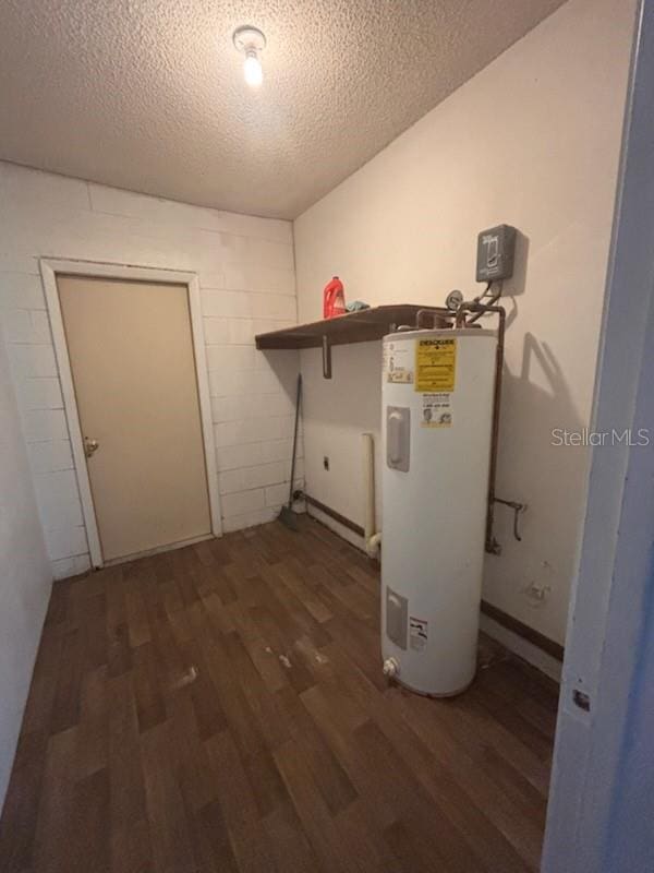 laundry area featuring laundry area, a textured ceiling, wood finished floors, concrete block wall, and water heater