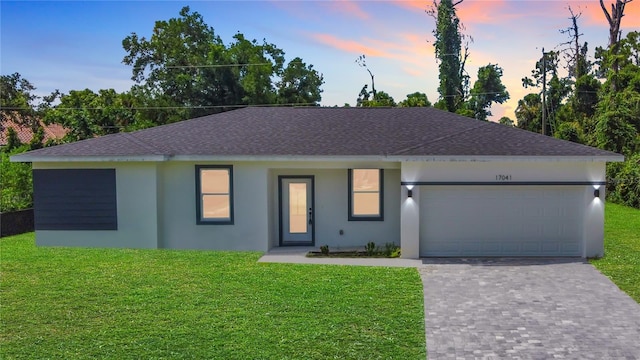 ranch-style home with decorative driveway, an attached garage, stucco siding, a lawn, and a shingled roof