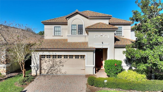 mediterranean / spanish house with stucco siding, decorative driveway, and a garage