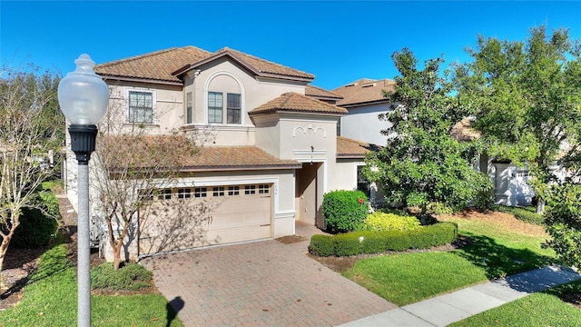 mediterranean / spanish-style house featuring stucco siding, a tile roof, a garage, and decorative driveway