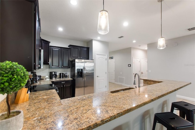 kitchen with visible vents, stainless steel fridge, light stone countertops, recessed lighting, and a sink