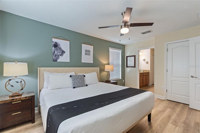 bedroom featuring baseboards, ensuite bath, ceiling fan, light wood-style flooring, and visible vents