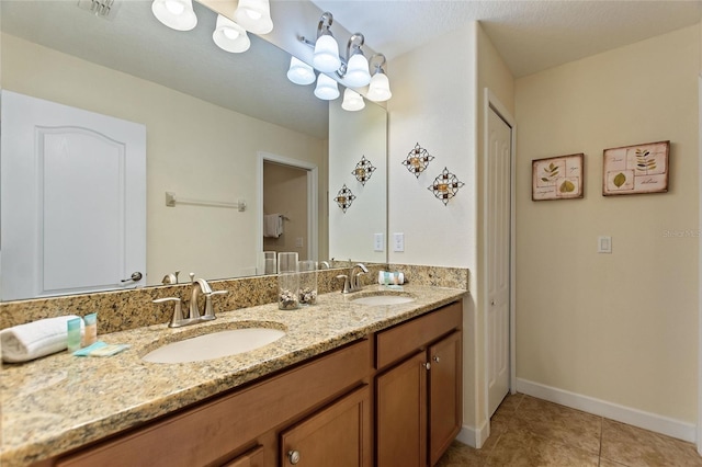 bathroom with double vanity, a sink, tile patterned floors, and baseboards