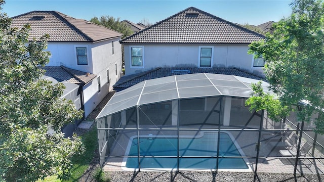 back of property featuring a lanai, an outdoor pool, a tiled roof, and stucco siding