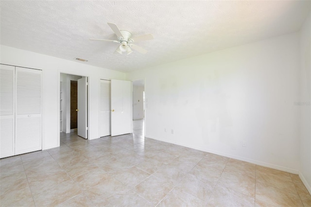 554 NW Twylite Ter, Port St Lucie, FL 34983 - unfurnished bedroom featuring baseboards, two closets, ceiling fan, light tile patterned floors, and a textured ceiling