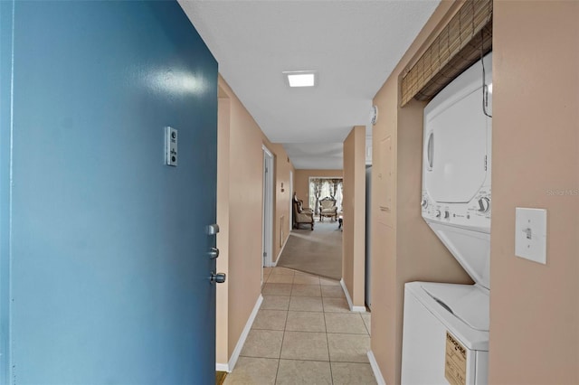 corridor with light tile patterned flooring, baseboards, and stacked washer / drying machine