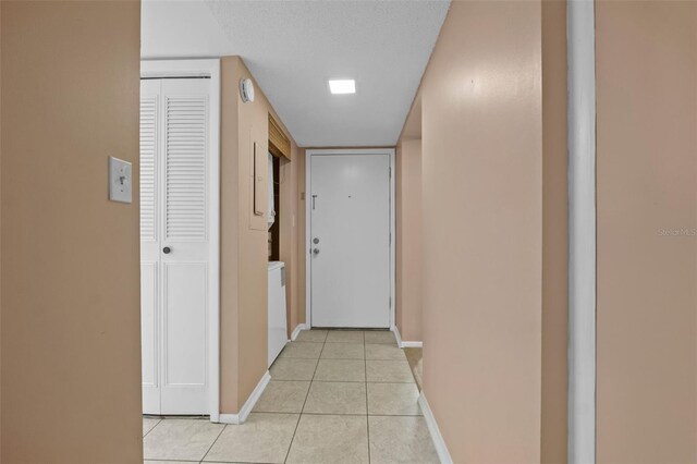 hallway featuring light tile patterned flooring, a textured ceiling, and baseboards