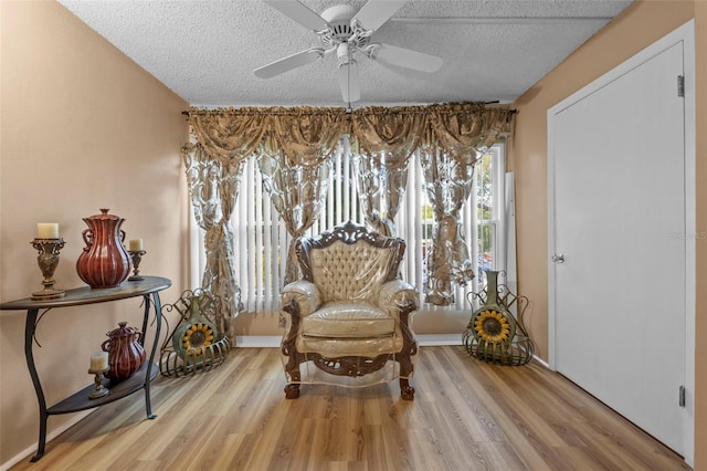 living area featuring baseboards, a ceiling fan, wood finished floors, and a textured ceiling