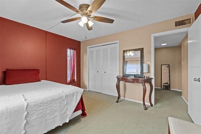 bedroom with a closet, a textured ceiling, light colored carpet, visible vents, and ceiling fan