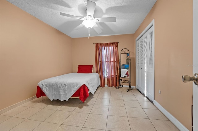 bedroom with a closet, a textured ceiling, baseboards, and light tile patterned floors