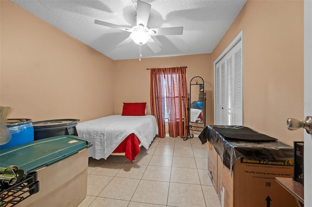 bedroom featuring light tile patterned flooring, a ceiling fan, a closet, and a textured ceiling