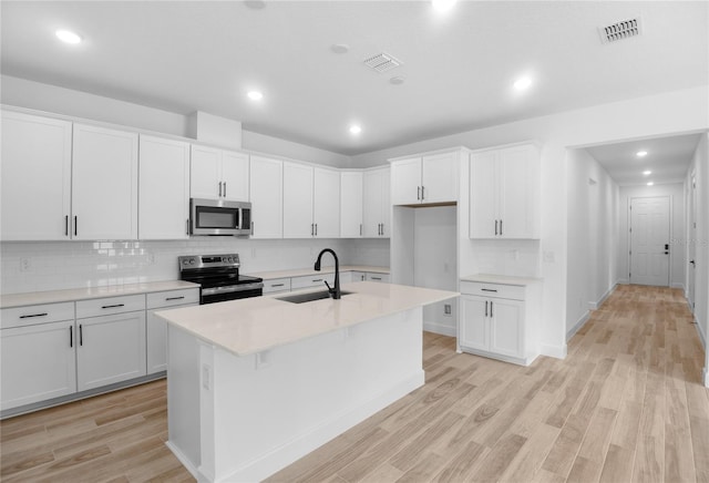 4083 Bannock Ave, Tavares, FL 32778 - kitchen featuring stainless steel appliances, a kitchen island with sink, decorative backsplash, light wood-style flooring, and light countertops