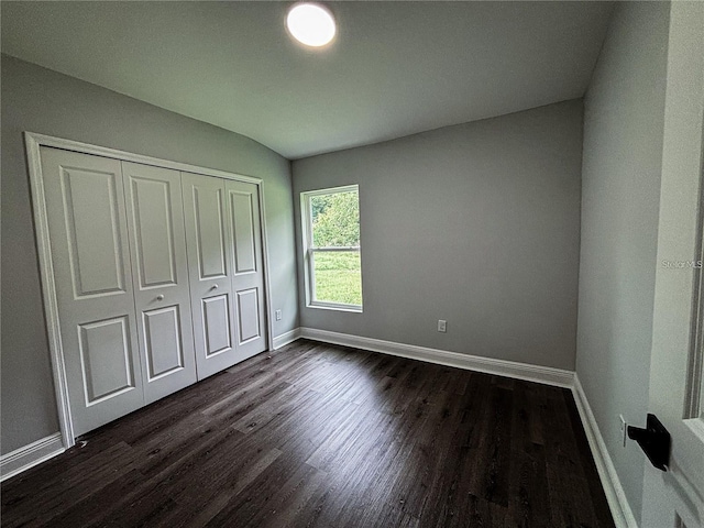 unfurnished bedroom with baseboards, vaulted ceiling, a closet, and dark wood-type flooring