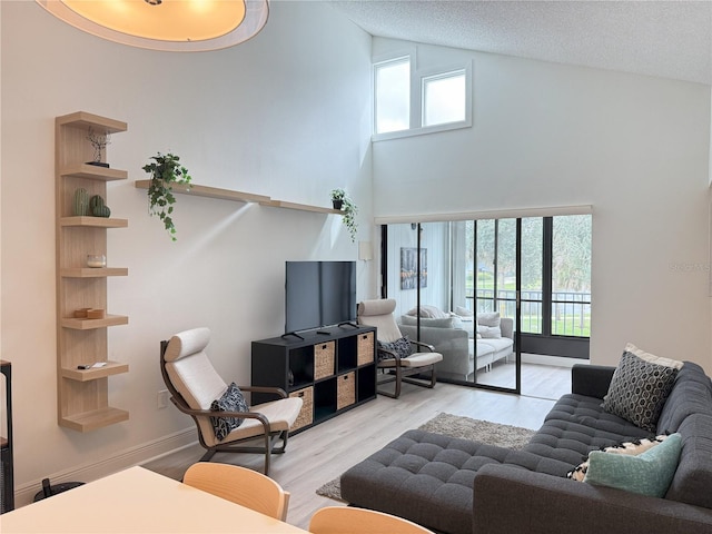 living area with baseboards, high vaulted ceiling, wood finished floors, and a textured ceiling