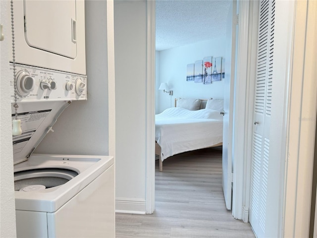 clothes washing area with stacked washer and clothes dryer, baseboards, a textured ceiling, light wood finished floors, and laundry area
