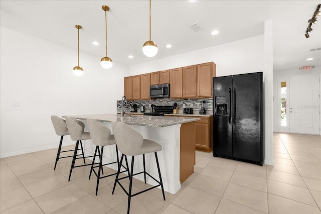 kitchen featuring tasteful backsplash, black fridge, stainless steel microwave, range, and a kitchen island with sink