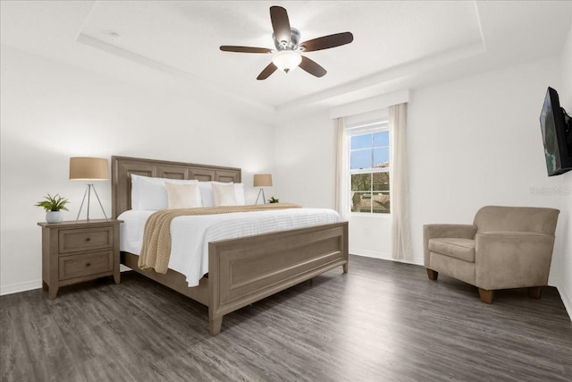 bedroom with baseboards, ceiling fan, dark wood-type flooring, and a raised ceiling